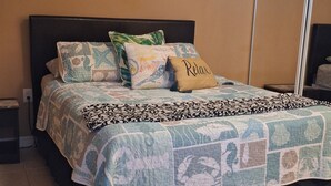 Un dormitorio con cama, ventilador de techo, mesita de noche y un cuadro en la pared.