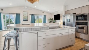 A modern kitchen with a central island, stainless steel appliances, and a large window with curtains. - Pet-Friendly, Close to beach access & town, Large - 2100 sq ft! Afternoon Delight! (Folly Beach)