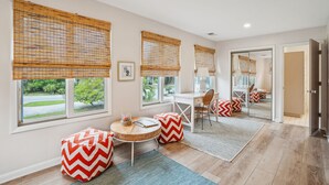 A modern room with large windows, a desk, a chair, and a small round table with a chair. - Pet-Friendly, Close to beach access & town, Large - 2100 sq ft! Afternoon Delight! (Folly Beach)