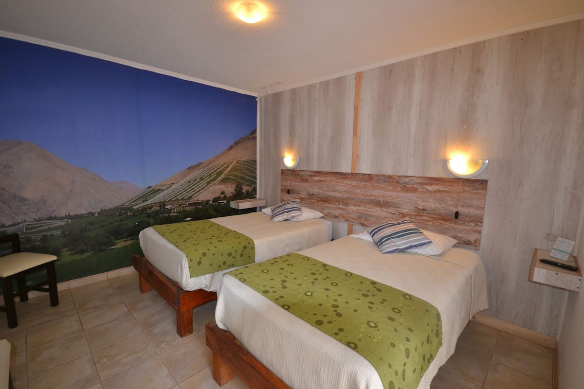 Ein Hotelzimmer mit zwei Betten, einem Wandgemälde einer Landschaft und einem Holzkopfstück.