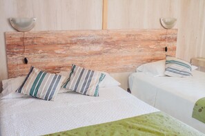 Quarto com cabeceira de madeira rústica, duas camas com almofadas listradas e um cobertor verde.