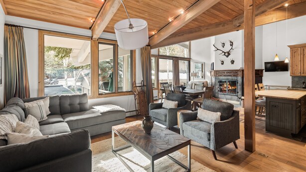 Ein geräumiges Wohnzimmer mit einer großen Couch, Sesseln und einem Couchtisch. Ein Kamin ist vorhanden, darüber ein Fernseher, und es gibt eine Essecke mit Holzmöbeln.