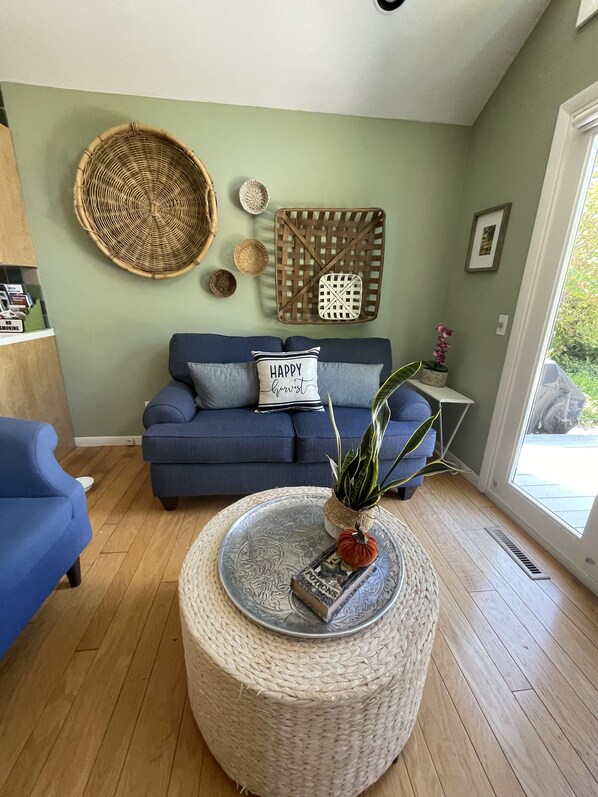 A living room with a blue sofa, a round woven coffee table, and a green wall.