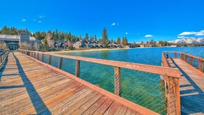 A wooden pier extending into a clear blue lake, surrounded by houses and a mountain in the background.