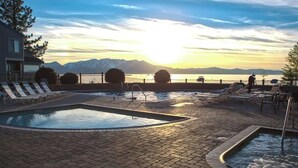 A pool area with lounge chairs, a small pool, and a view of mountains and a body of water during sunset.