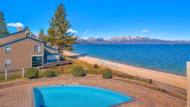 A modern house with a swimming pool, a beach, and a mountain range in the background.