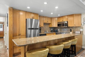 Eine Küche mit Holzschränken, Edelstahlgeräten und Arbeitsplatten aus Granit, sowie Barhocker.