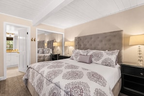 A bedroom with a large bed, a mirror, a wardrobe, and a nightstand with a lamp.