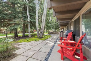 Eine überdachte Terrasse mit roten Adirondack-Stühlen, einem Grill und einer Steinmauer.