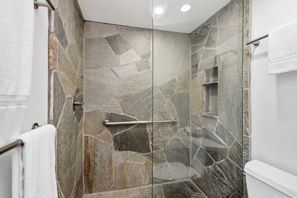 Un baño moderno con cabina de ducha de piedra, puerta de cristal y un inodoro blanco.