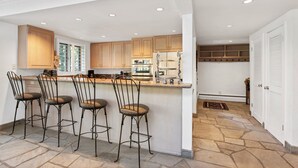 Una cocina moderna con armarios de madera, una isla central con taburetes de bar y suelo de piedra.