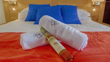 Una cama bien tendida con almohadas blancas y azules, una manta roja y una botella de perfume sobre una toalla blanca.