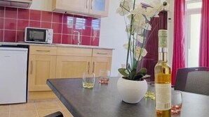 Eine moderne Küche mit Mikrowelle, Kühlschrank und einem Esstisch. Auf dem Tisch steht eine Weinflasche, eine Pflanze und zwei Gläser. Ein rotes Sofa und ein Gemälde sind an der Wand zu sehen.