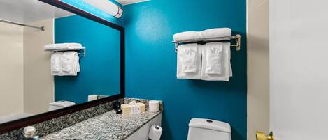 Un baño con pared azul, encimera de granito, lavabo blanco, inodoro y espejo con toallero.
