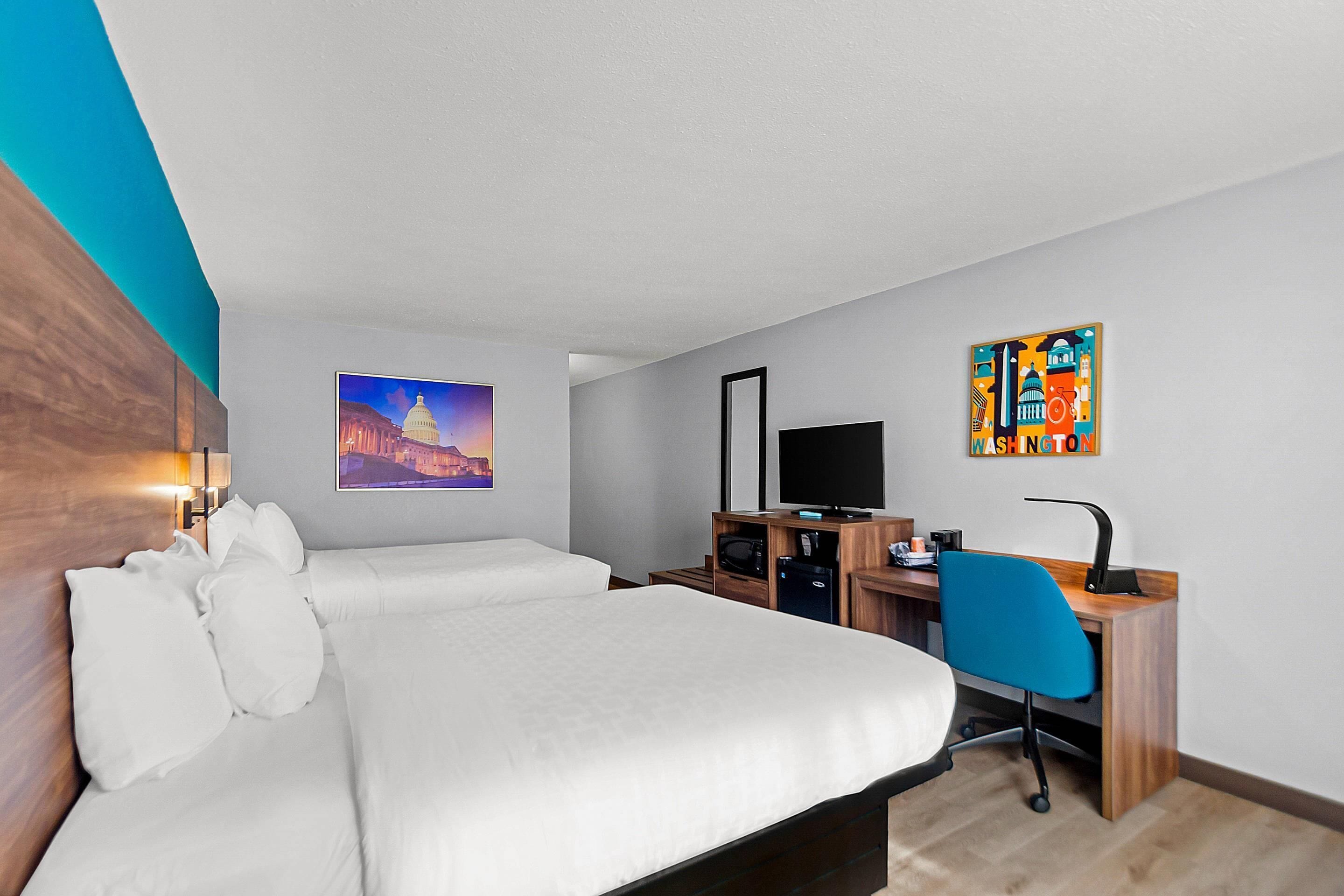 A hotel room with a bed, a desk, a chair, a television, and artwork on the walls.