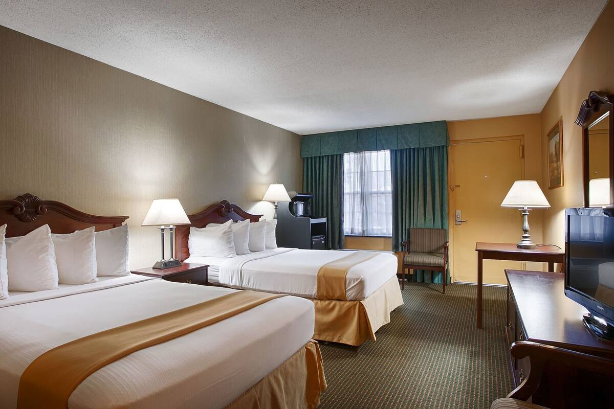 A hotel room with two beds, a desk, a television, and a chair.