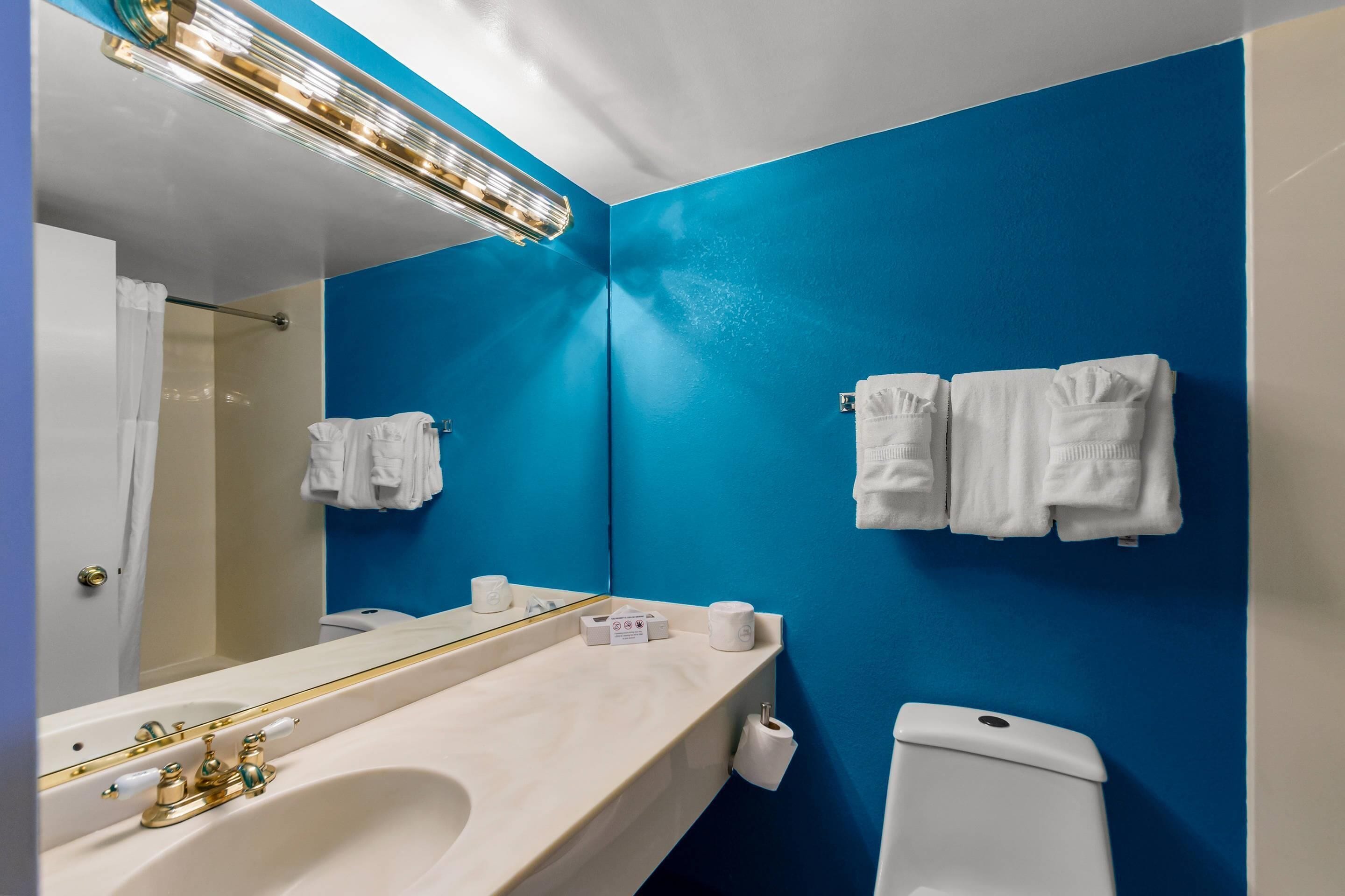 A bathroom with a blue wall, a white sink, a mirror, and two white towels hanging on the wall.