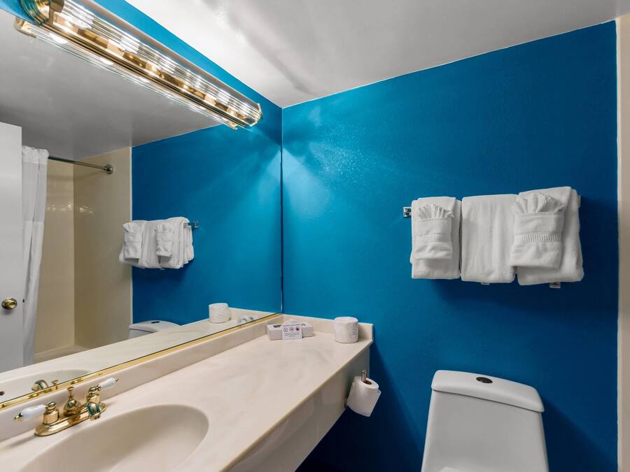 Un baño con pared azul, un lavabo blanco, un espejo y dos toallas blancas colgadas en la pared.