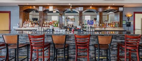 A bar area with multiple stools, a counter with various bottles, and a television mounted on the wall.