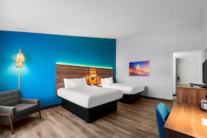 Una habitación de hotel con dos camas, un escritorio, una silla y un cuadro en la pared.