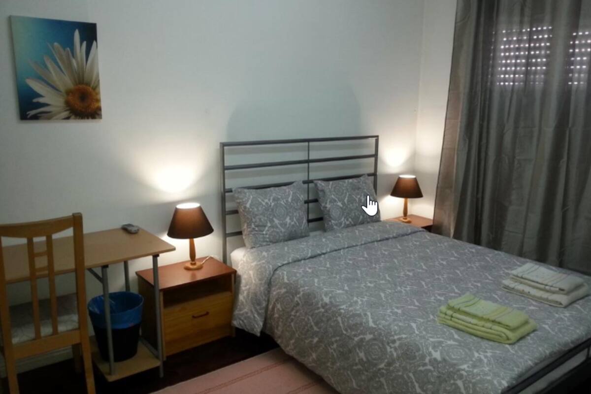 Un dormitorio con una cama, dos mesitas de noche con lámparas, una silla, un escritorio y un cuadro en la pared.