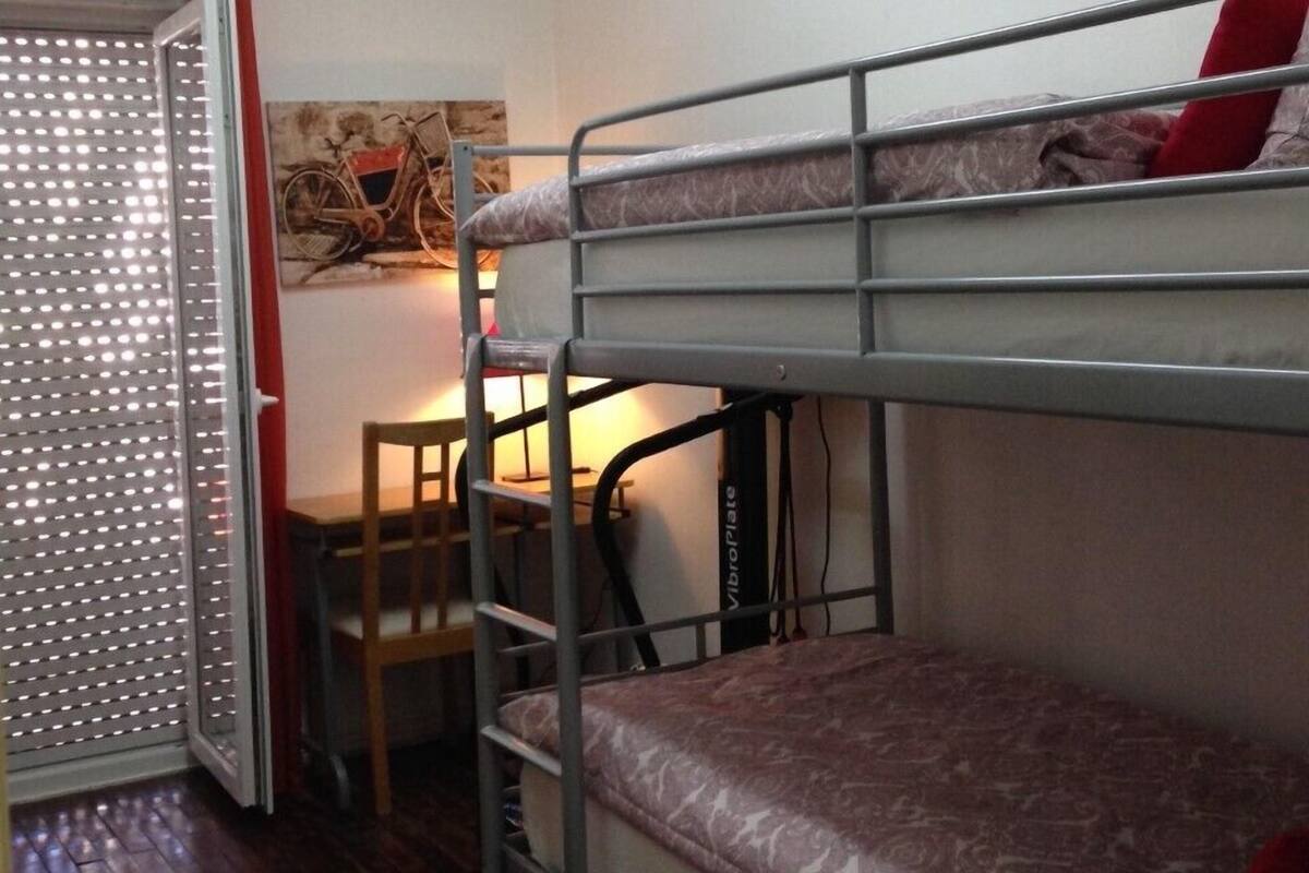 Habitación con literas, un escritorio y una silla, un cuadro de una bicicleta en la pared y una ventana con persianas.