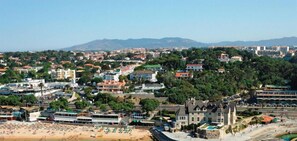 Un pueblo costero con playa, edificios residenciales y una gran propiedad con piscina.