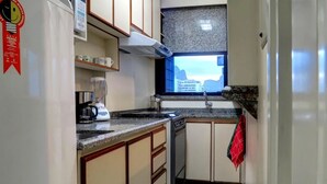 Una cucina compatta con piano cottura a gas, una macchina per il caffè e una finestra vista edifici.