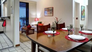 Zona pranzo con tavolo in legno apparecchiato per quattro persone, sottopiatti rossi e una lampada rossa su un tavolino.