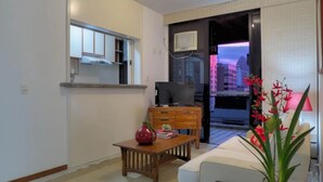 Un soggiorno moderno con un divano, un tavolino in legno, una TV e vista sulla città attraverso una porta scorrevole.