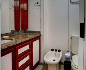 Une salle de bain avec un lavabo blanc, des meubles rouges, un bidet et des toilettes.