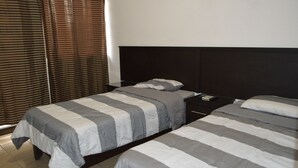 Een hotelkamer met twee bedden, een donker hoofdeinde en een raam met luxaflex.