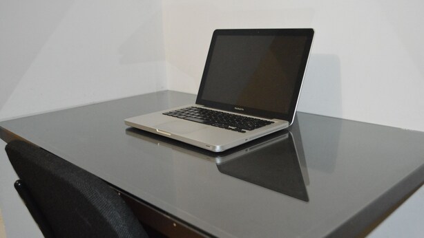 Een laptop op een glazen tafel, met een stoel ernaast.