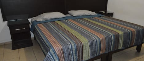 A bed with a striped bedspread, a black nightstand, and a black headboard.