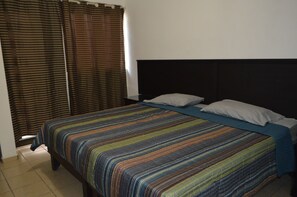 Ein Bett mit gestreifter Bettdecke, zwei Kissen und einem Kopfteil in einem Zimmer mit Vorhängen.