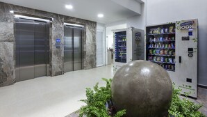 A lobby with marble walls, two elevators, a large decorative sphere, and vending machines. - Torca Hotel (Cali)