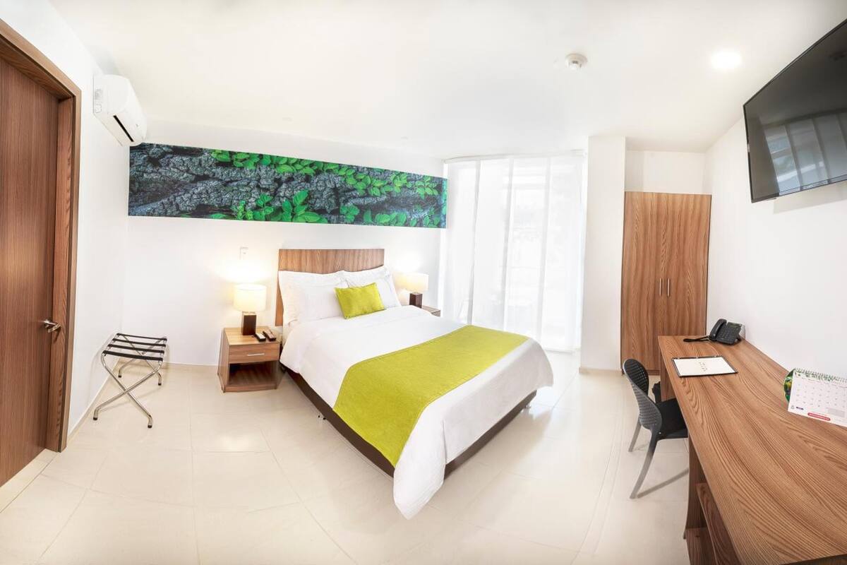 A hotel room with a bed, bedside tables, a desk, a chair, a TV, and a large window.