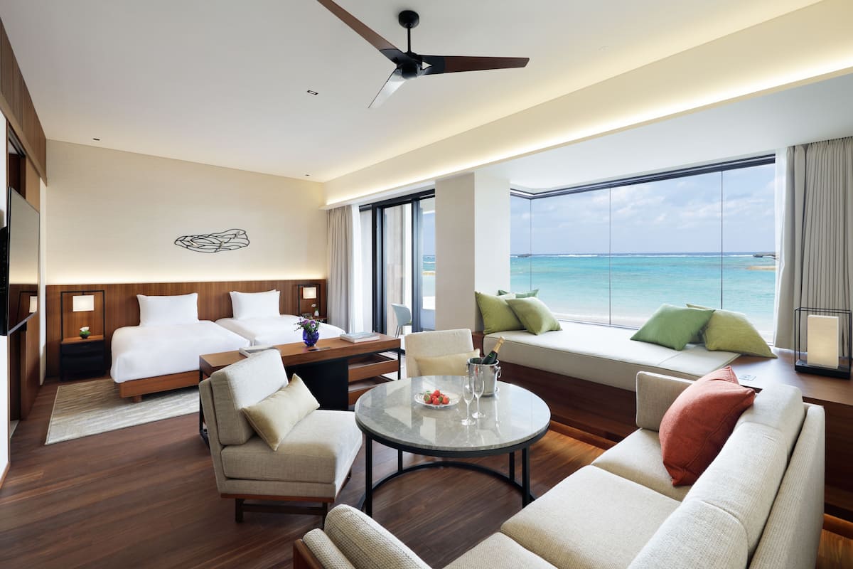 A hotel room with a bed, a sofa, a dining table, and a view of the ocean.