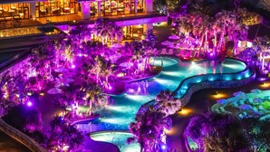 Un complexe hôtelier doté de plusieurs piscines, de palmiers et d’un bâtiment aux grandes fenêtres.