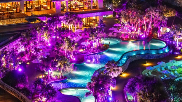 Un complexe hôtelier doté de plusieurs piscines, de palmiers et d’un bâtiment aux grandes fenêtres.