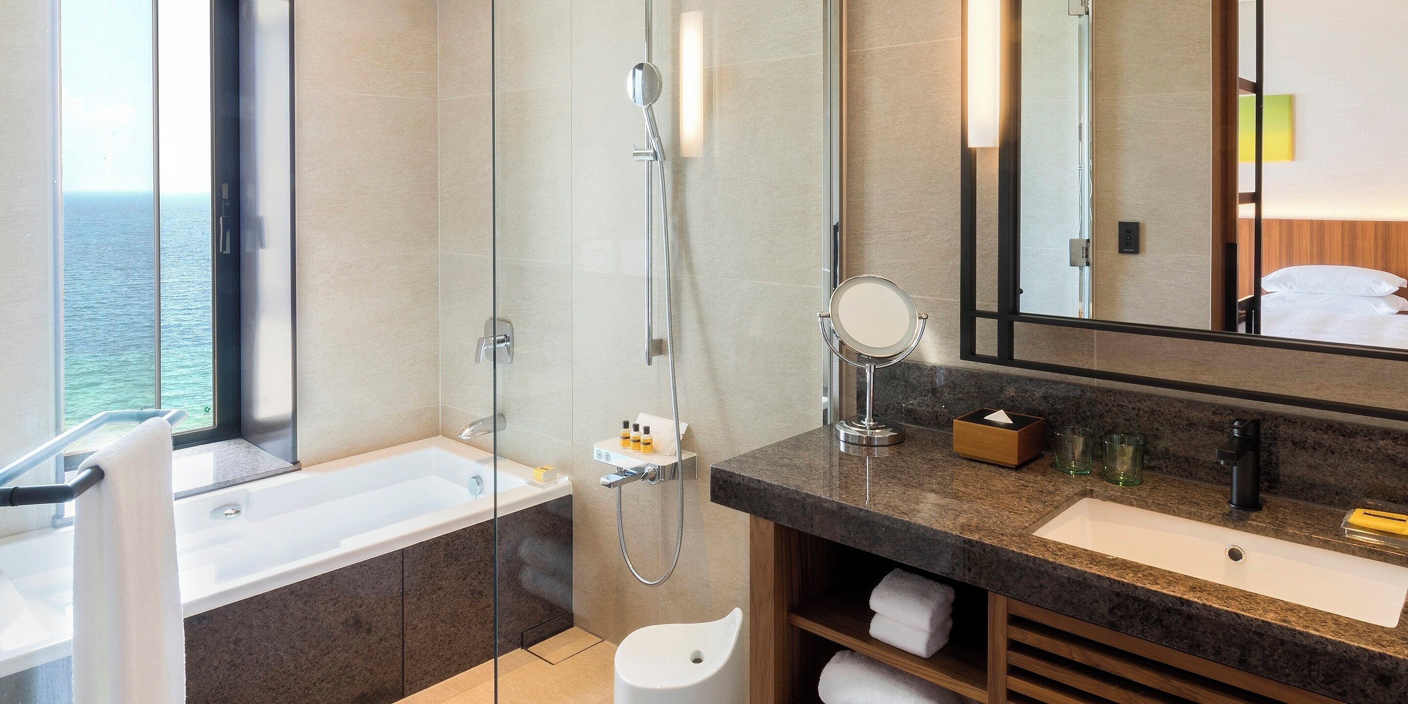 Un baño moderno con bañera, ducha y lavabo. Hay un espejo grande sobre el lavabo y una ventana con vistas al mar.