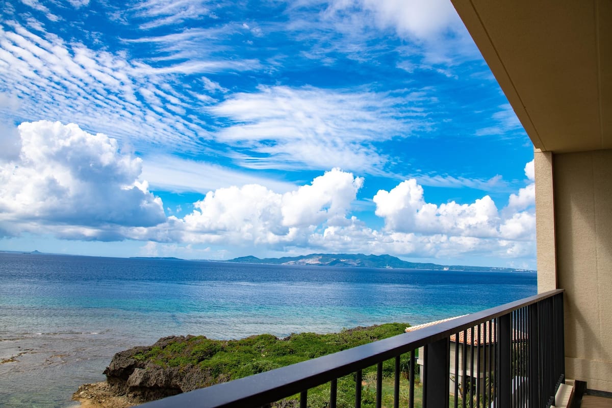 A balcony with a view of the ocean and distant mountains.