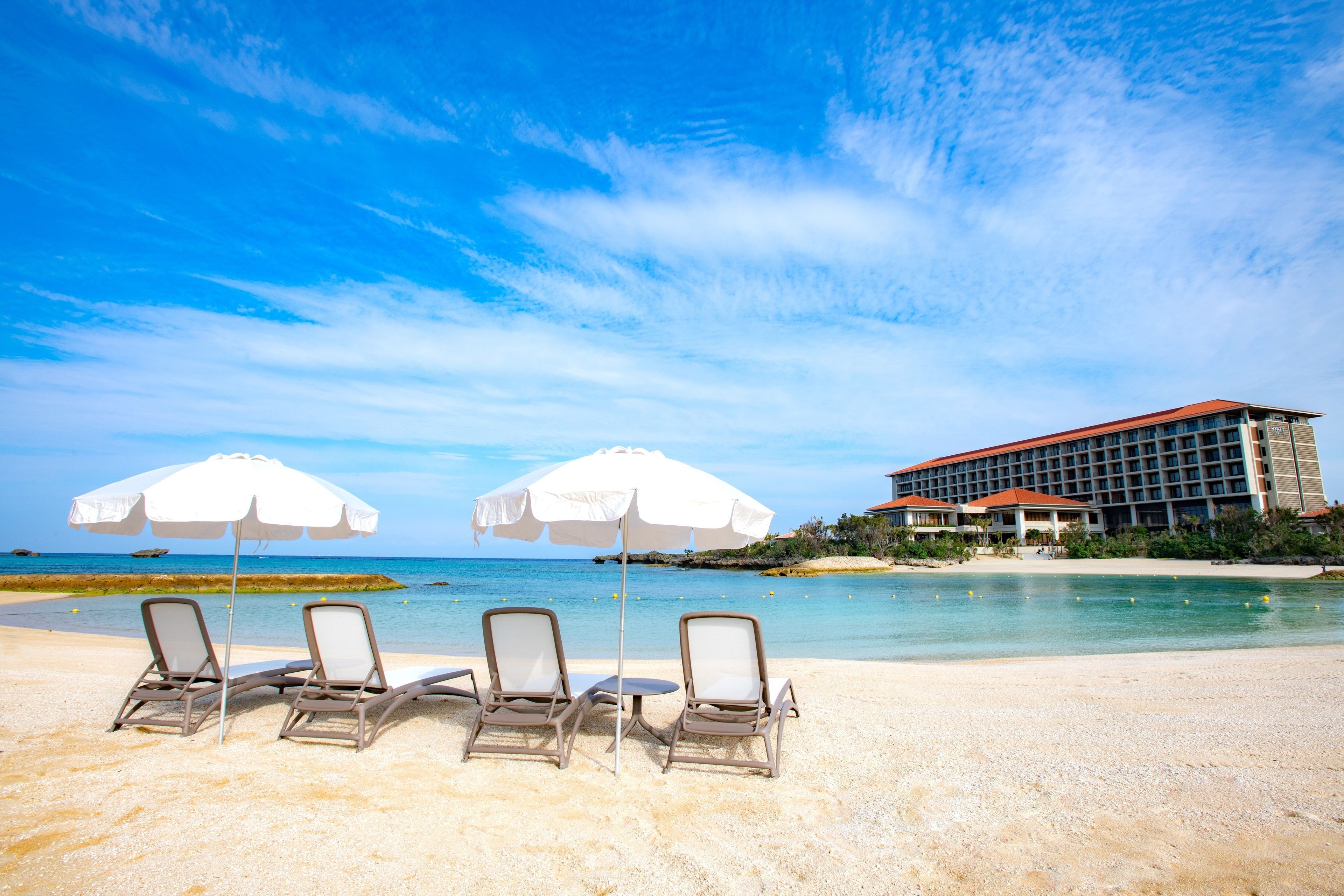 A beach with lounge chairs and umbrellas, a hotel building in the background, and a clear blue sky.