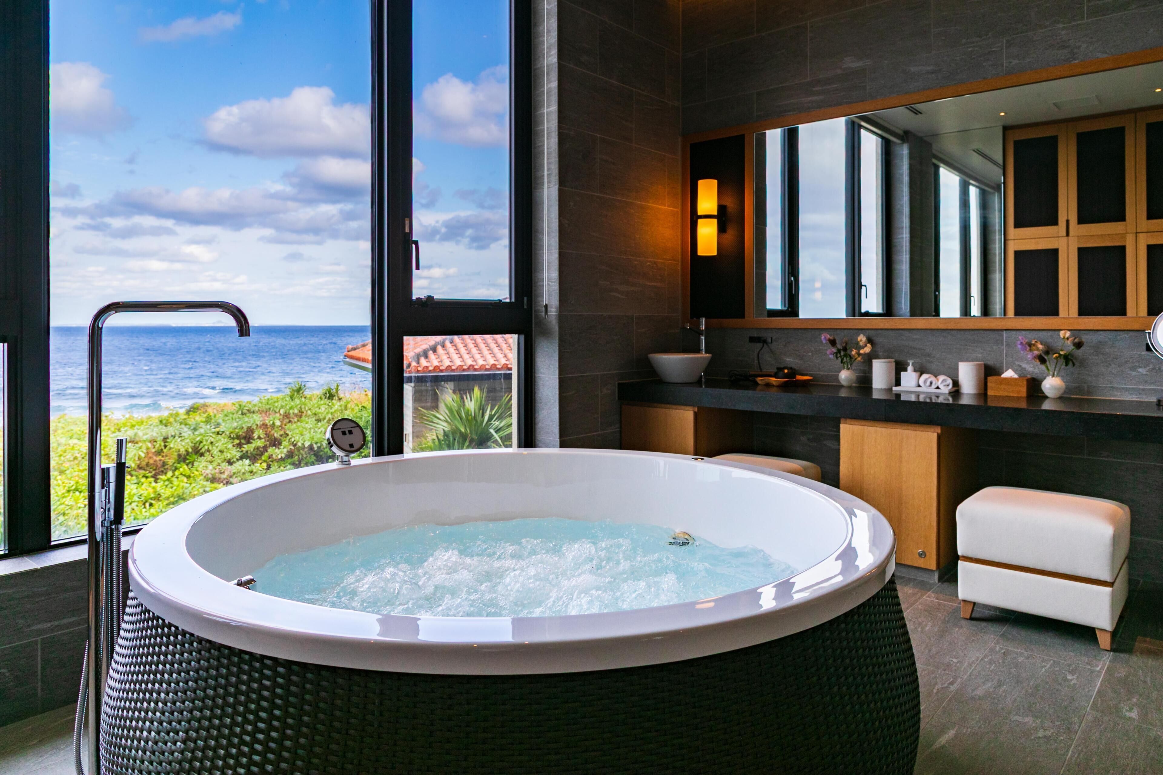 Un baño moderno con una bañera grande, un tocador con espejo y vistas al océano.