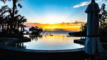 Une piscine avec vue sur le coucher de soleil, des palmiers et une statue.