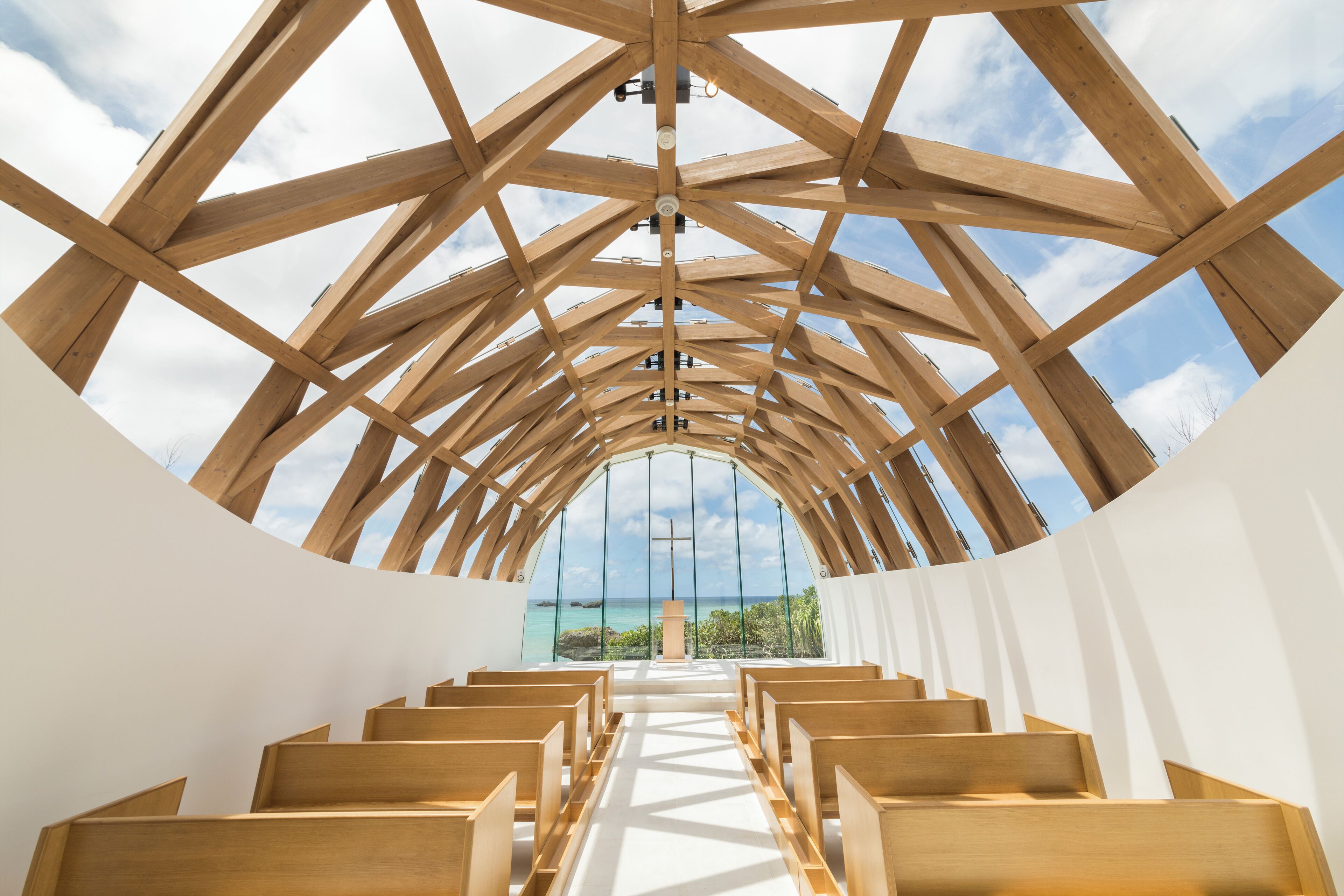 A church interior with wooden beams, pews, and a view of the ocean.