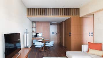 A modern hotel room with a dining area, kitchenette, and a sofa with orange pillows.