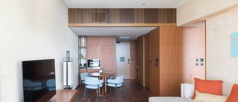A modern hotel room with a dining area, kitchenette, and a sofa with orange pillows.