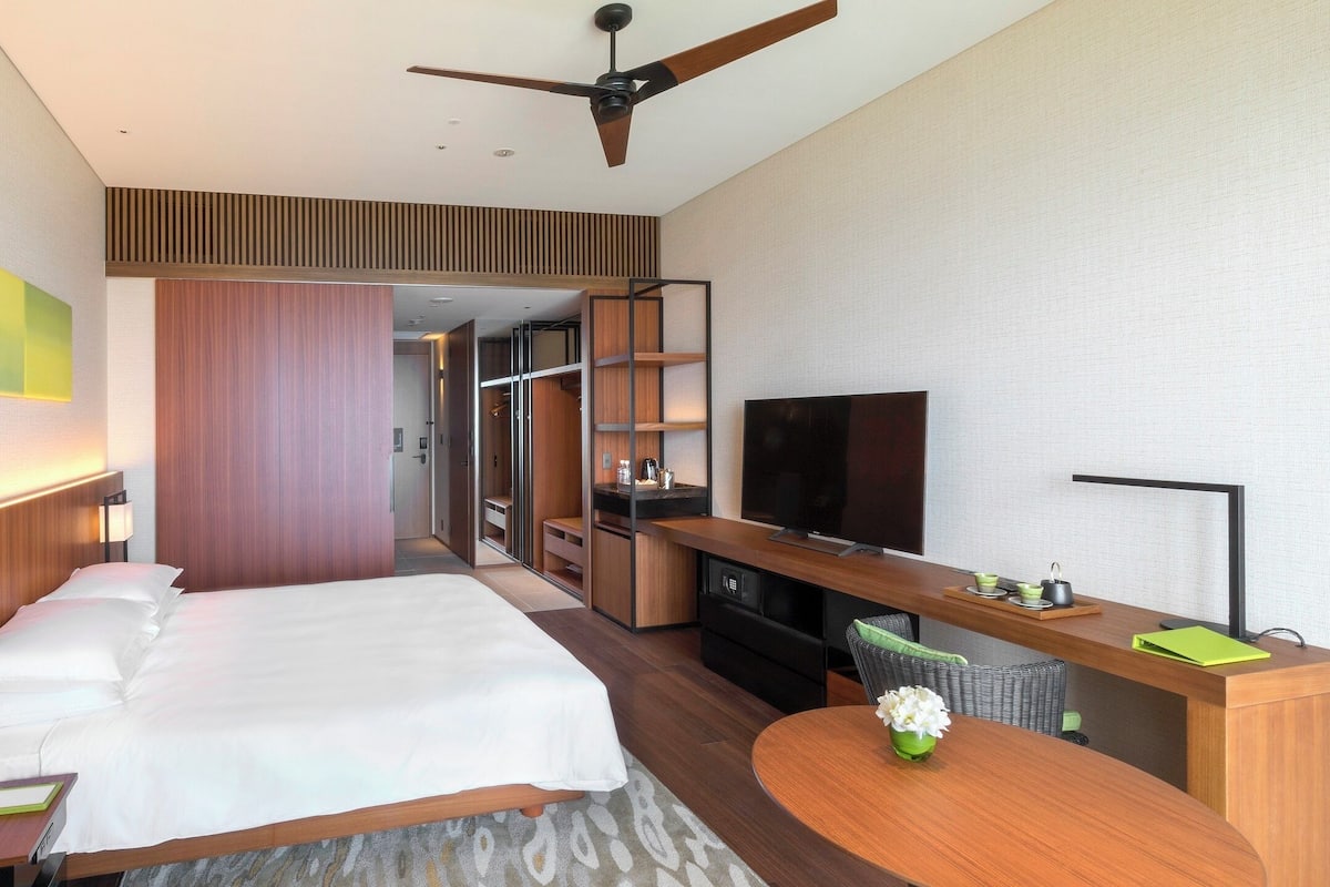 A hotel room with a bed, desk, TV, and a ceiling fan.