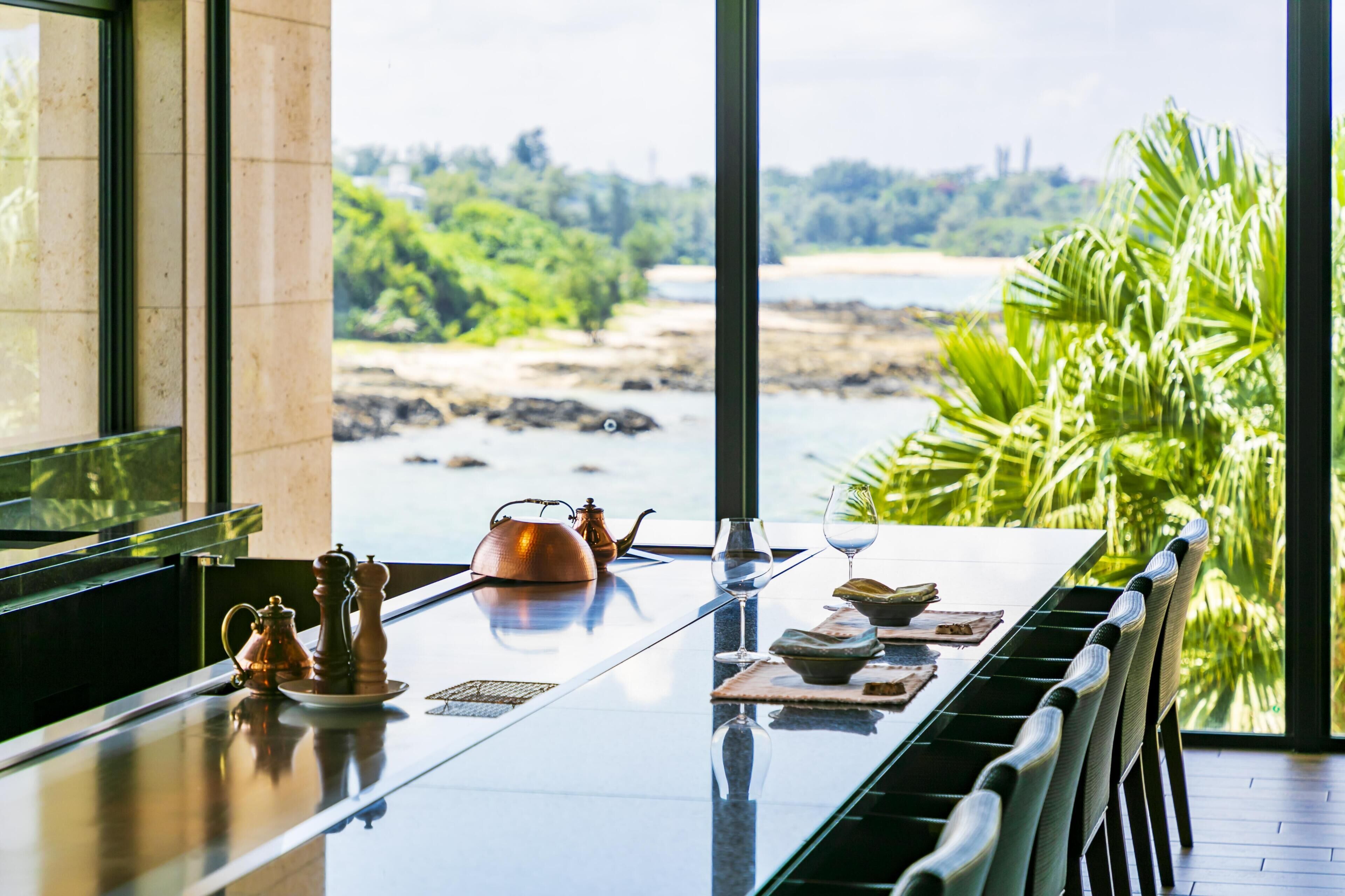 A dining table with a view of a beach and greenery.